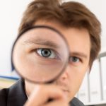 A businessman looking through a magnifying glass.