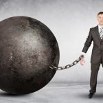 A businessman attached to a large ball and chain.