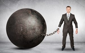 A businessman attached to a large ball and chain.