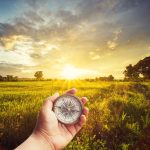 A man holding compass on hand at field and sunset for navigation guide.