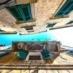 The narrow street of the ancient city, looking up at the open window with wooden shutters under a beautiful aged balcony, collapsing yellow wall with cracks. Kotor Old Town, Montenegro.