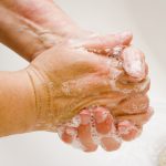 woman washing hand under running water white sink chrome spout