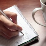 Womans hand with pen notebook and coffee