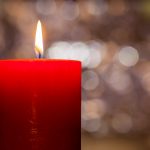 Candles light. Christmas candle burning at night. Abstract candle background. Golden light of candle flame. Closeup of a red candle with creamy bokeh background.