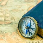 The compass beside a blue book with a cross on the cover. The compass and the book is on top of a navigational map