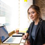 Confident woman with laptop in a cafe considers her web writing options.