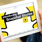 Close up of tablet open to Snapchat with text, "Introducing Snapchat Stories"