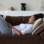 Happy woman reclines on her couch with laptop in hand