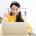 Young asian woman with headphones working at her laptop in virtual meeting.