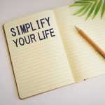 Open notebook with "Simplify Your Life" written on the left page with pencil and leaf