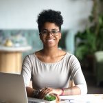 Head shot portrait of smiling African American woman sitting confidently at a desk with laptop nearby