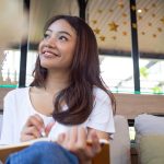 Smiling Asian woman holding a notebook and pen looks off to the side, thinking