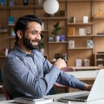 Relaxed Indian man chats with clients over video call in home office