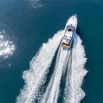 Motor boat glides through beautiful teal waters, aerial view, leaving behind crisp white wake