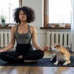Woman meditating in lotus pose on mat in apartment, with dog nearby