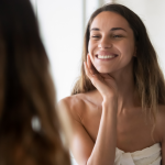 Young woman in a bath towel smiles at herself in the mirror