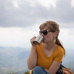 Woman in sunglasses drinks coffee on a hill