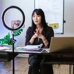 Professional woman using ring light and cell phone to record promotional vide at her desk