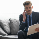 Businessman holds clipboard and talks on the phone, determined but tense