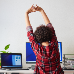 Working woman stretches her arms over her head from her desk