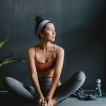 Woman in yoga gear calmly looks off in the distance, water bottle at her side, lotus pose