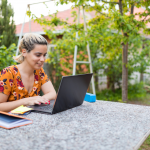 Woman working remotely from garden table smiles