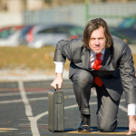 Man with suit and briefcase crouches at the track starting line