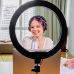 Content creator smiles at her iPhone tripod, shown through a Ring light with a microphone