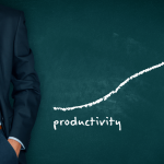 Businessman stands by a chalkboard that reads "productivity" and has an arrow going up