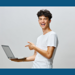 Young man smiles and points to laptop he is holding