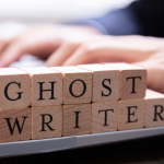 wooden blocks spell out "GHOST WRITER" next to a computer keyboard