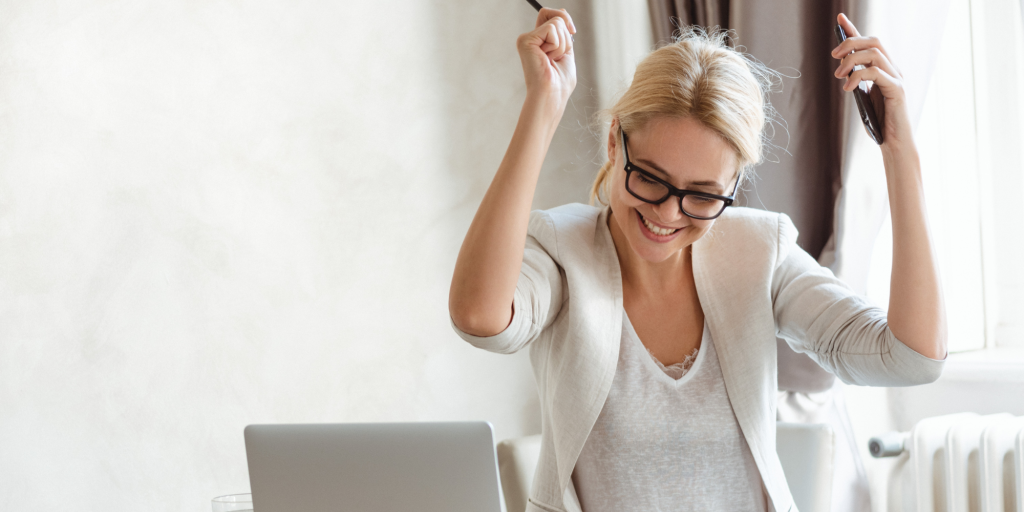 a woman raises her hands in triumph at her laptop